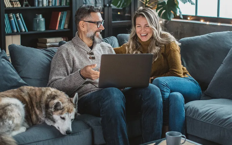 A couple with their dog looking at their laptop sitting on their sofa
