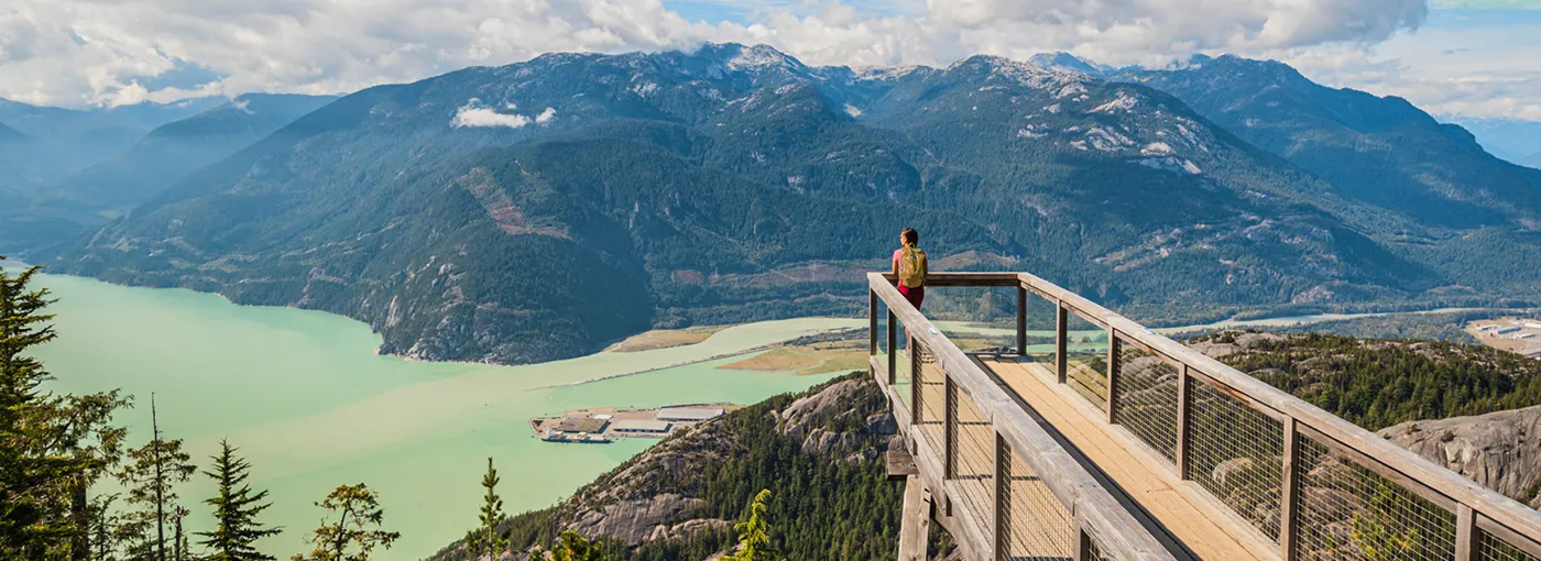 Woman at the peak of a hike looking out over a lake and mountain