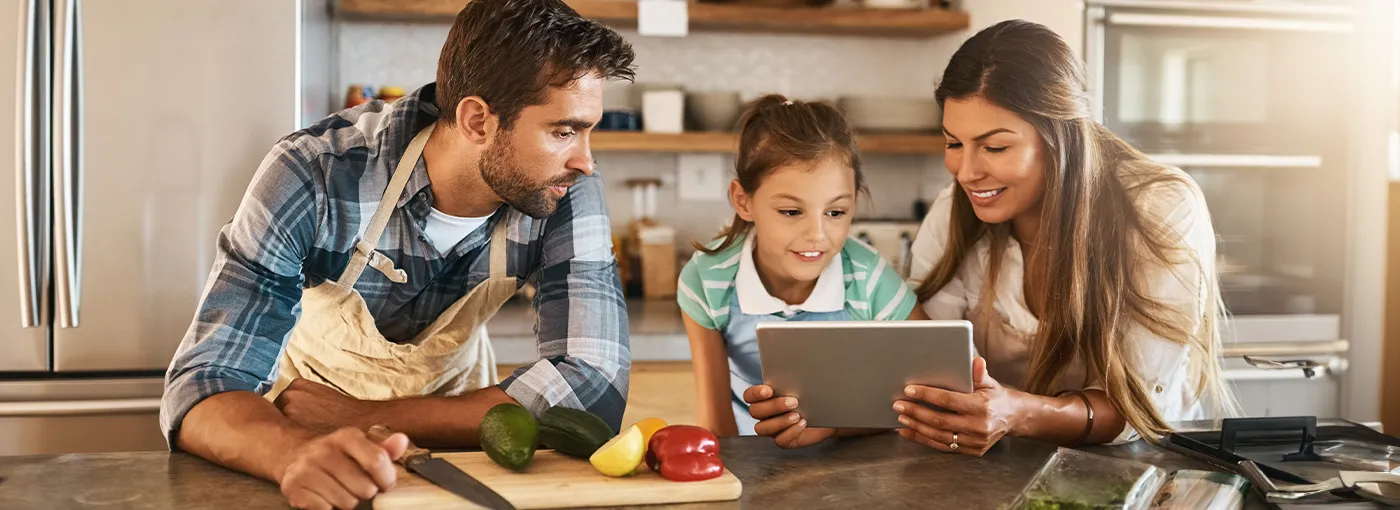 A family cooking together in the kitchen while looking at a tablet device