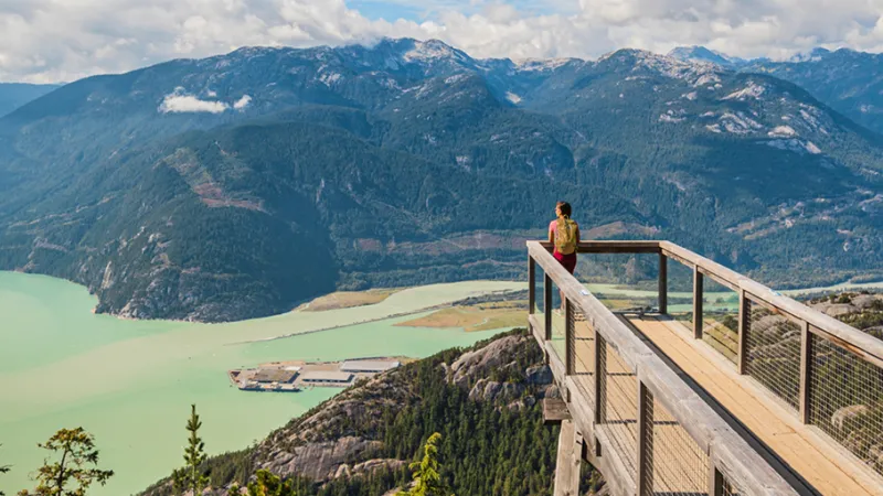 Woman at the peak of a hike looking out over a lake and mountain