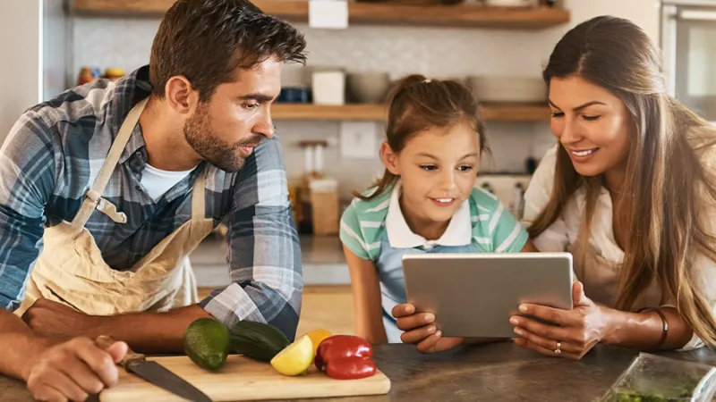 A family cooking together in the kitchen while looking at a tablet device